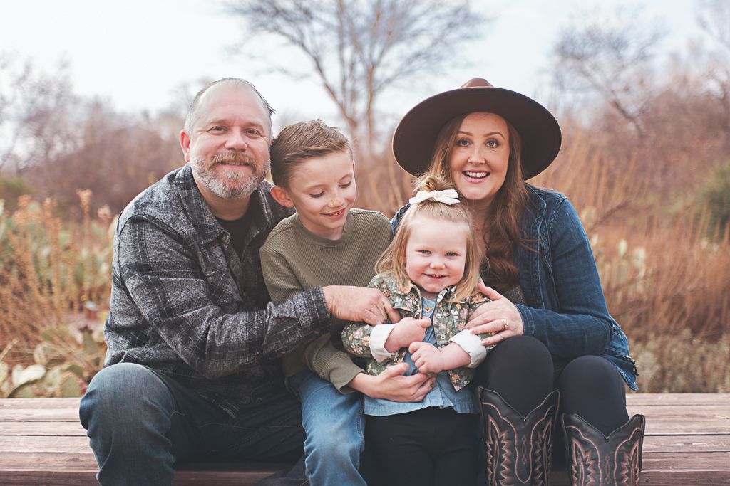 Smiling family of four posing together in a park, enjoying a sunny day outdoors