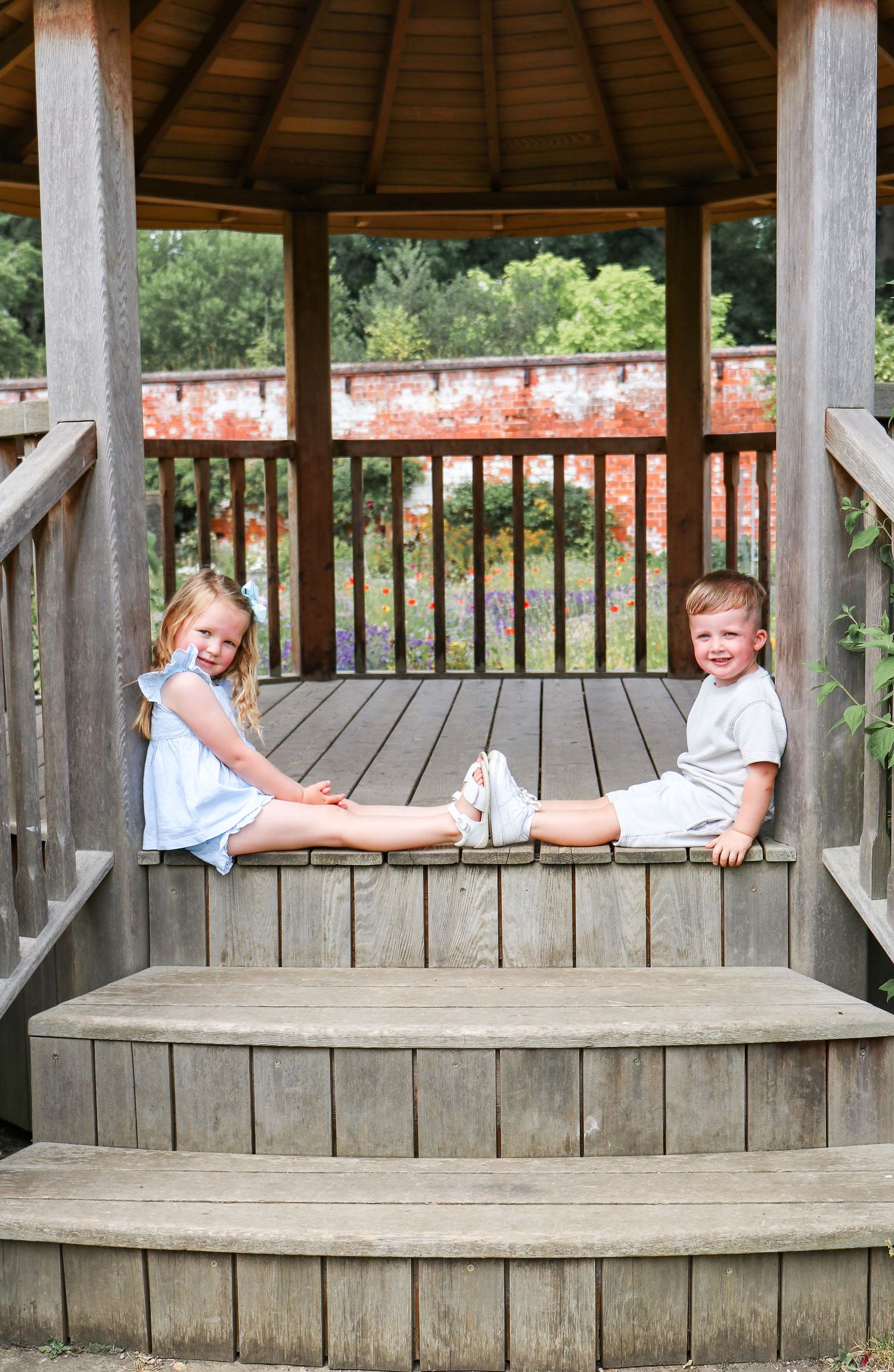Children sitting together on wooden steps with their feet touching in a playful pose at the park, during family shoot in Derbyshire