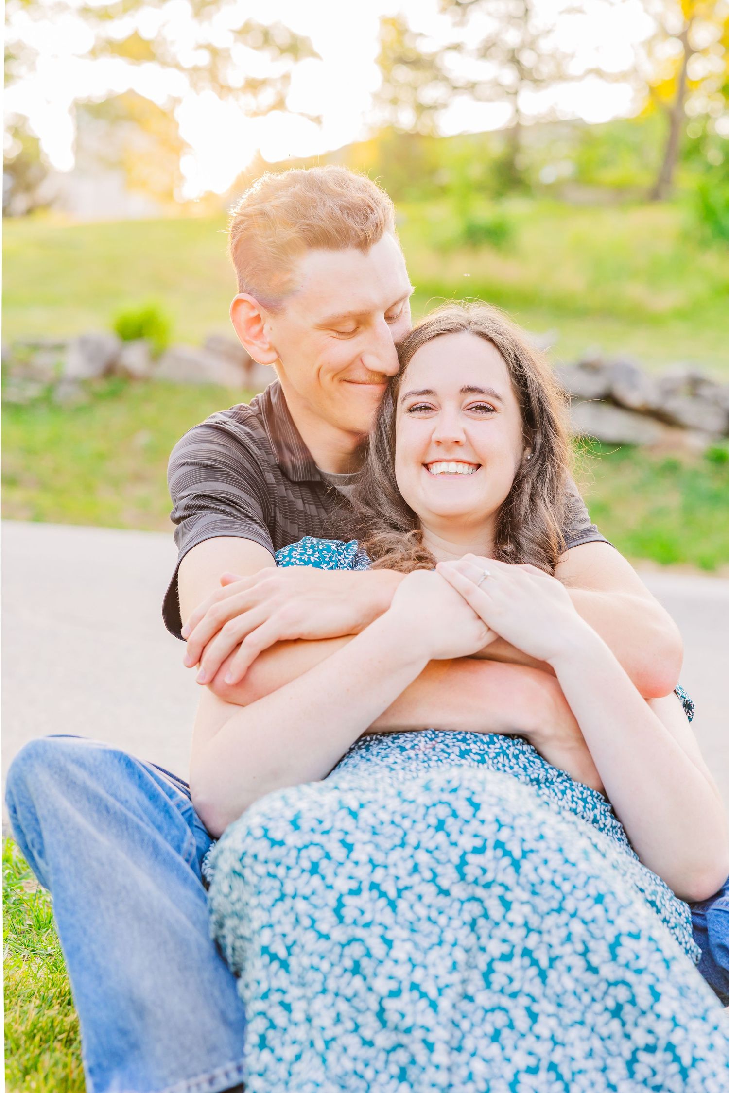 A couple shares a tender embrace while sitting on grass during a golden sunset.