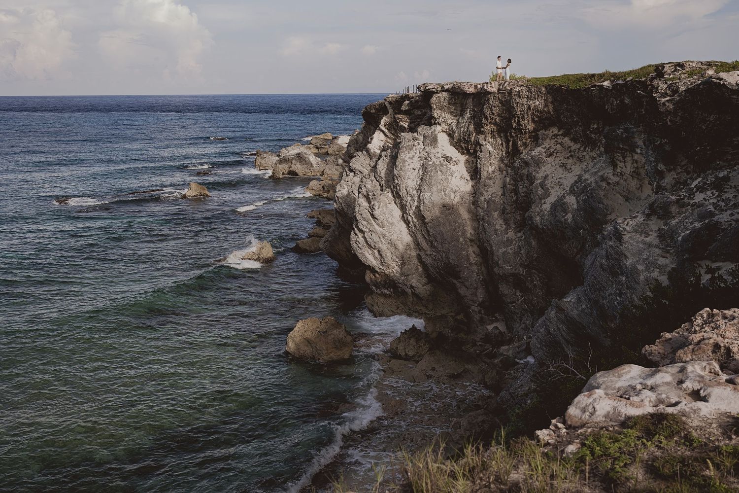 Dramatic white limestone cliffs rise above the turquoise ocean waters along a rugged coastal landscape.
