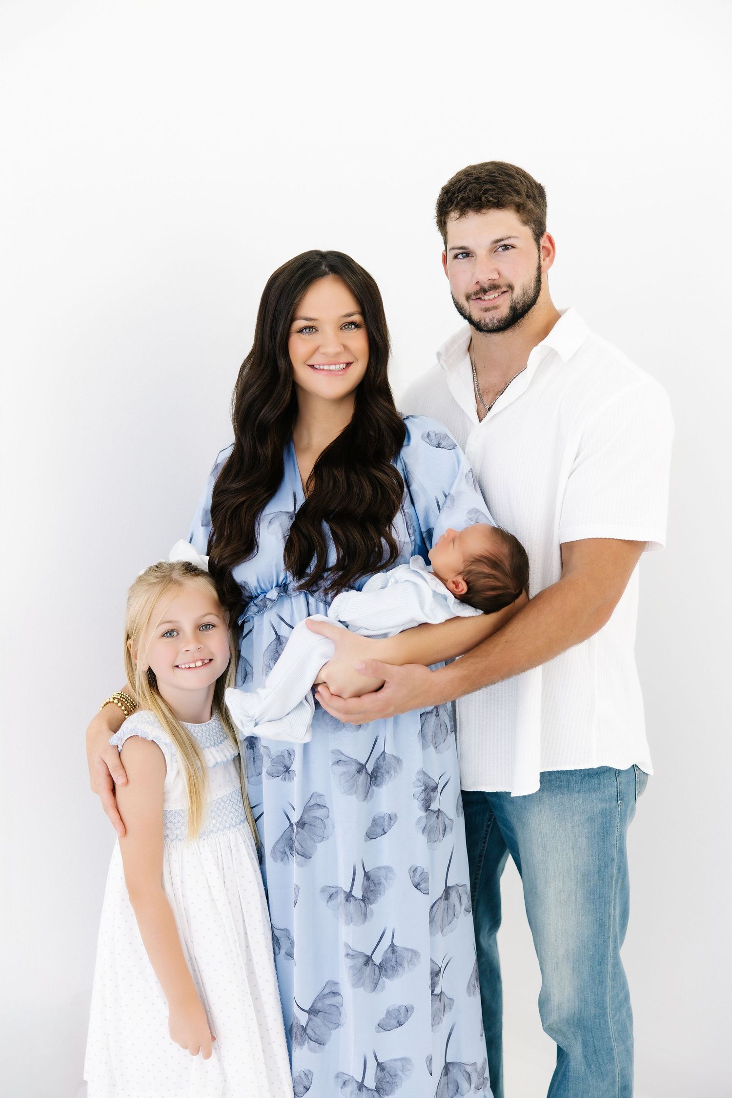 Family portrait against white background with parents in casual clothing and young girl in white dress.