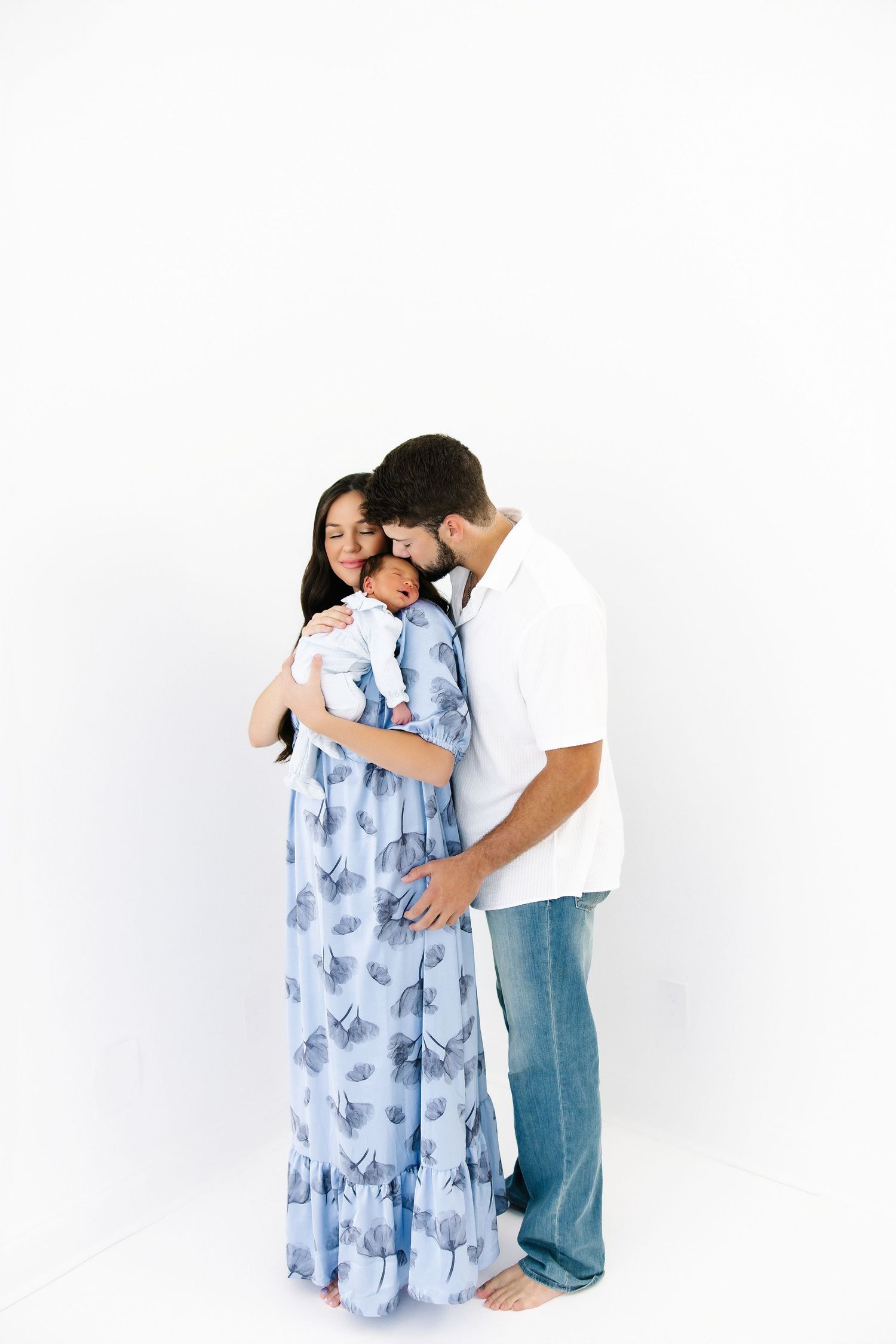 A couple embraces while wearing casual attire against a white studio background.