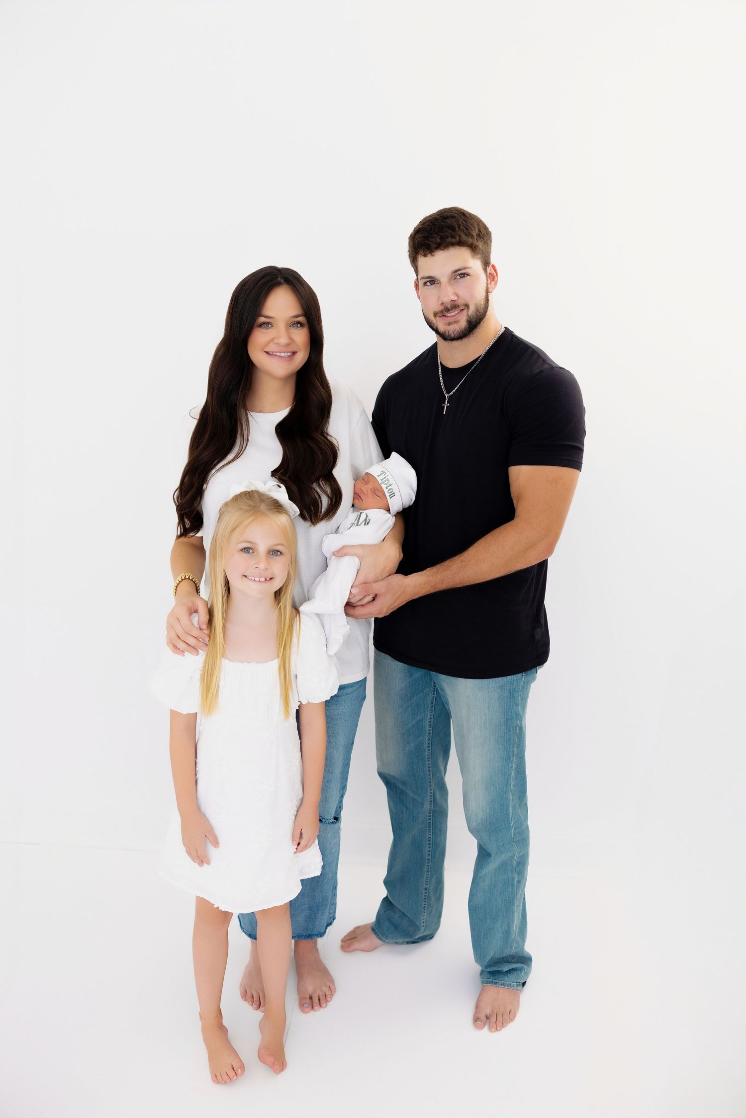 Family of four poses together in casual white and denim outfits against white background.