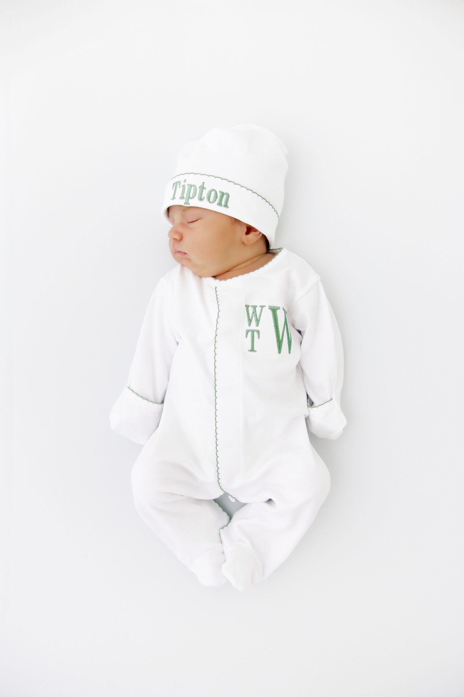 A sleeping newborn wearing white clothing and hat photographed against white background.