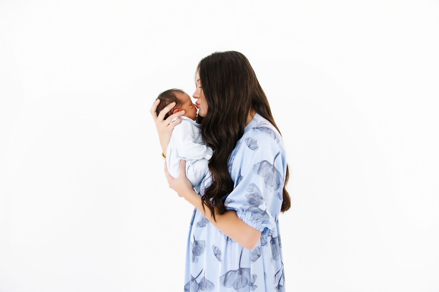 Someone wearing a light blue floral dress holds a baby on a white background.