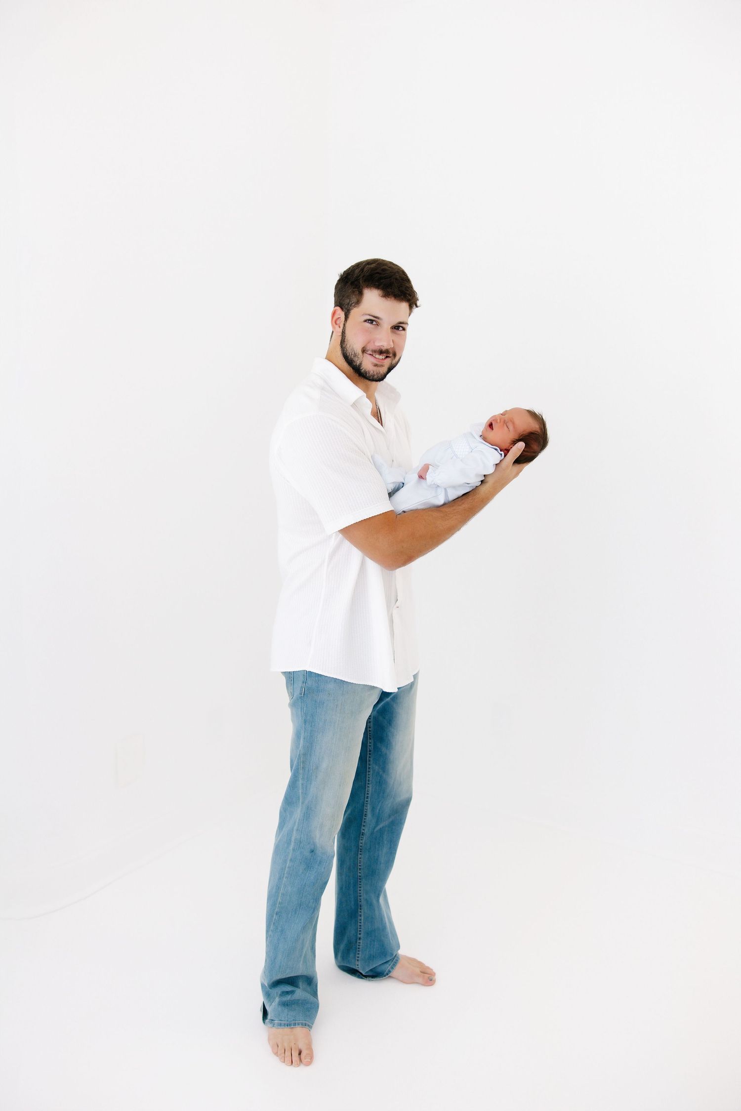 A person in jeans and white shirt stands playfully on a white studio backdrop.