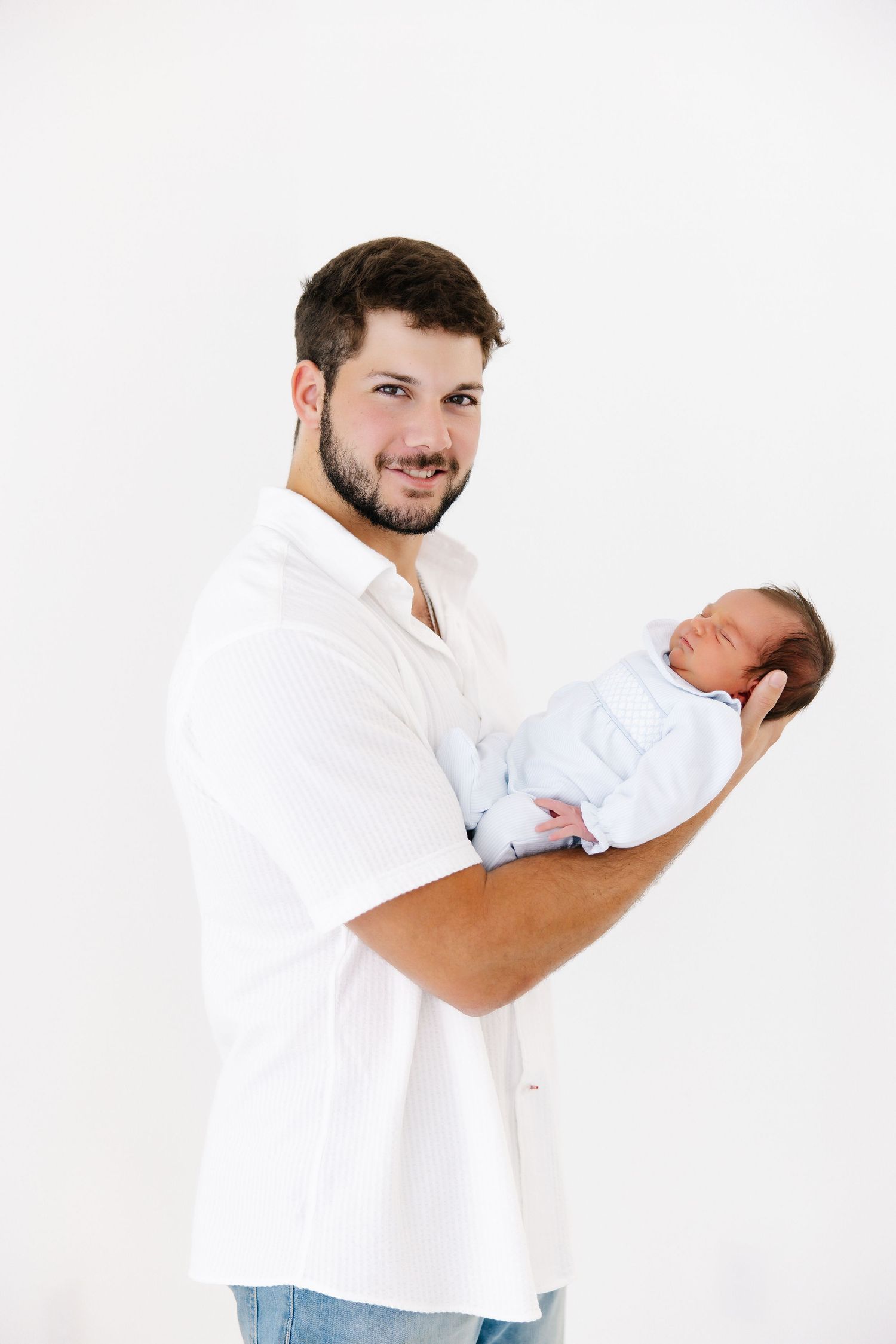 Parent in white shirt gently holds sleeping newborn against white studio backdrop.