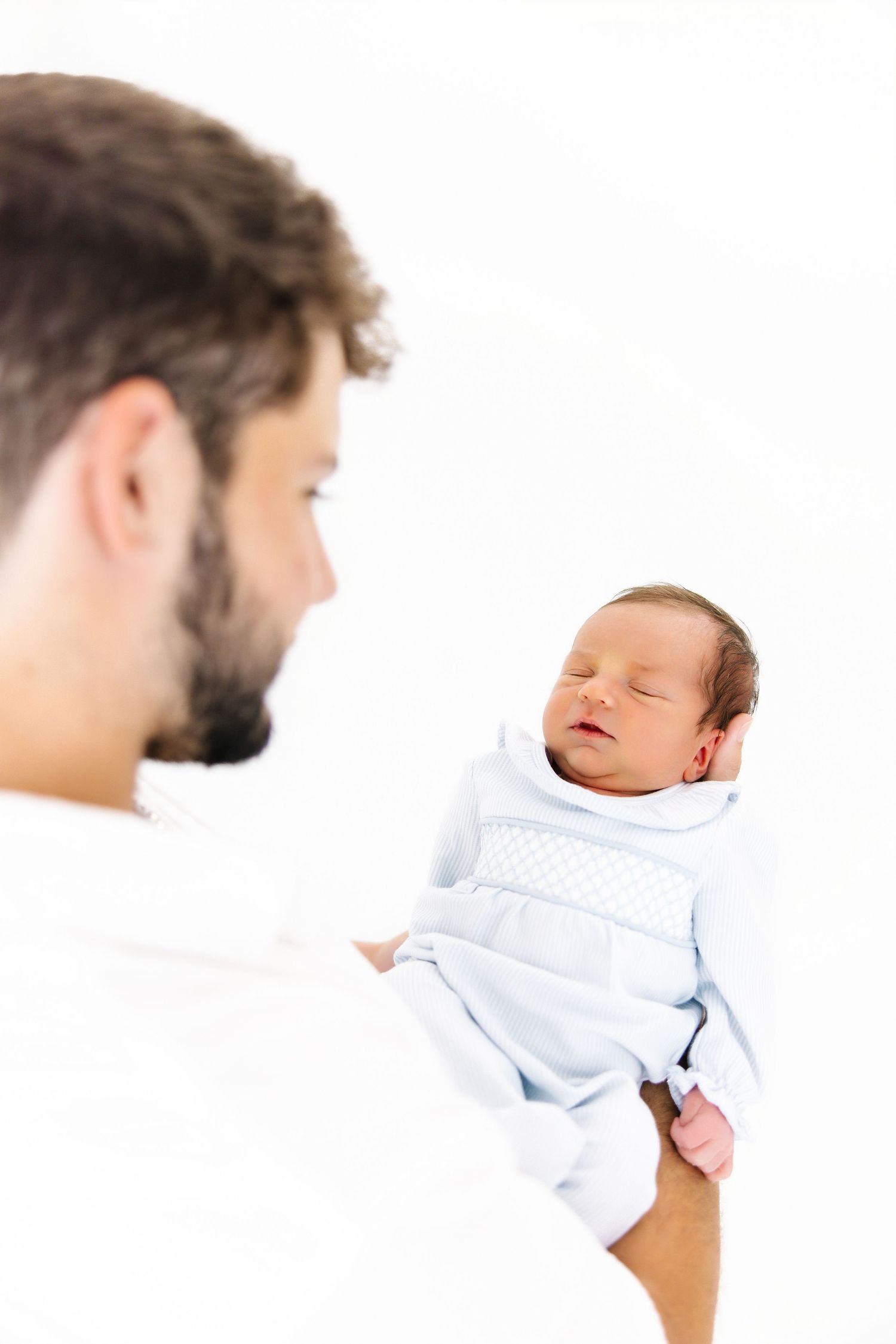 Series of shots showing a parent holding and bonding with a sleeping newborn baby in white.