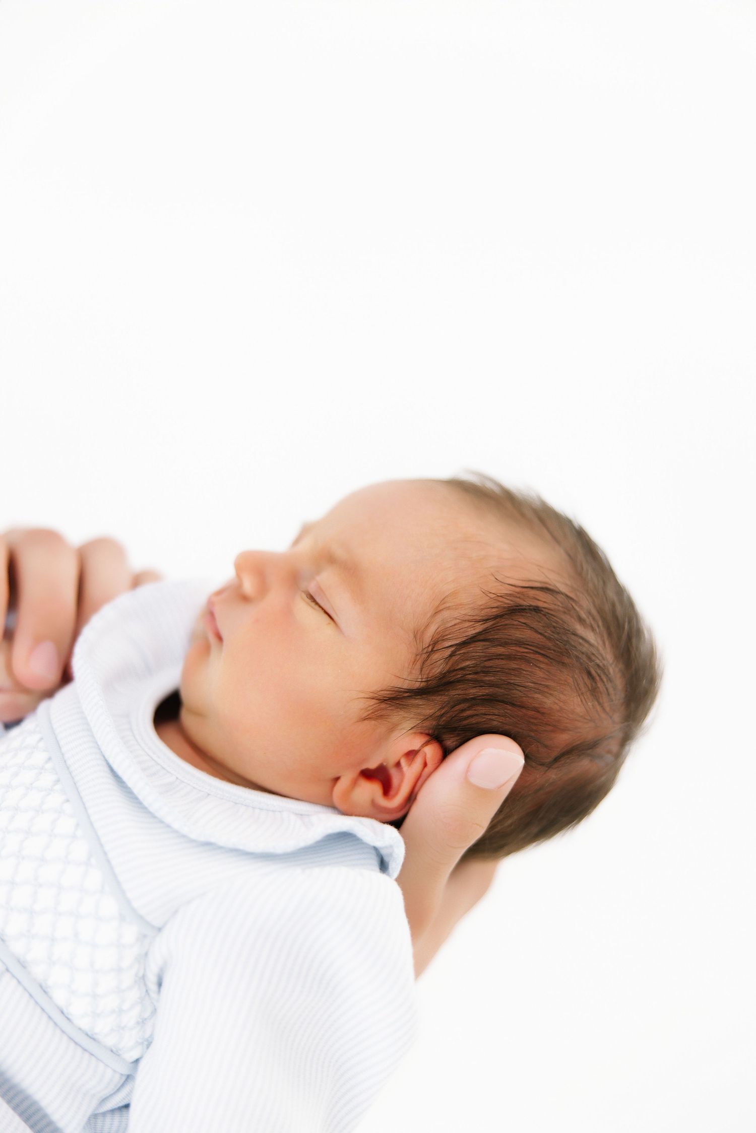 Close-up shots of a sleeping newborn baby wearing a white outfit against a pure white background.