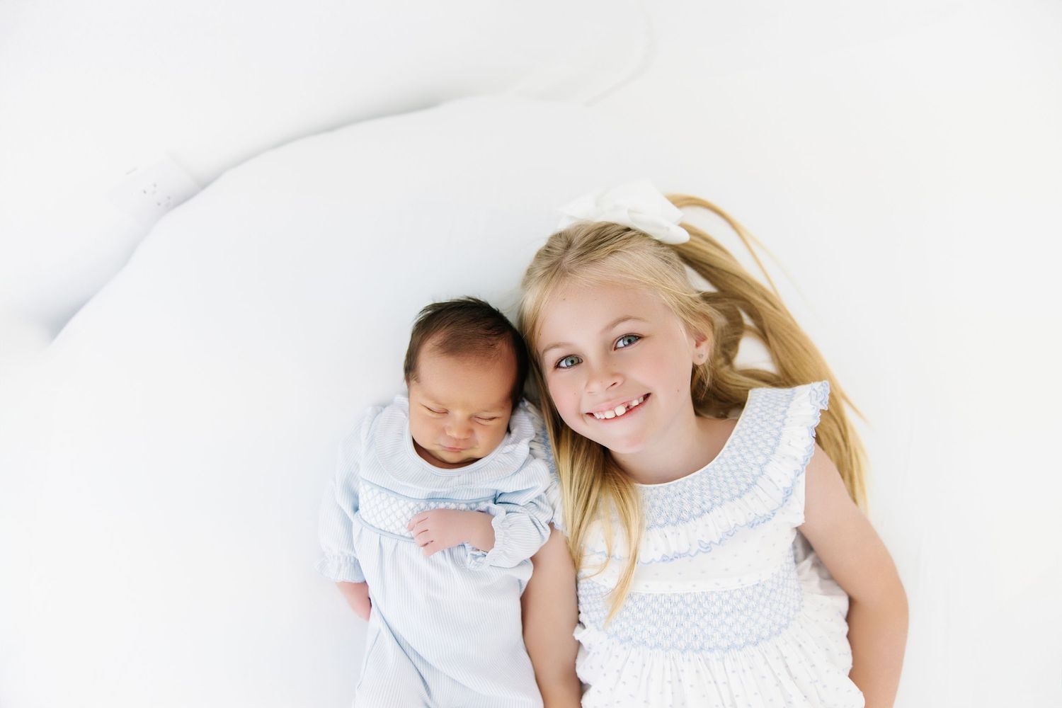 Two children laying on white bedding while playing and laughing together.