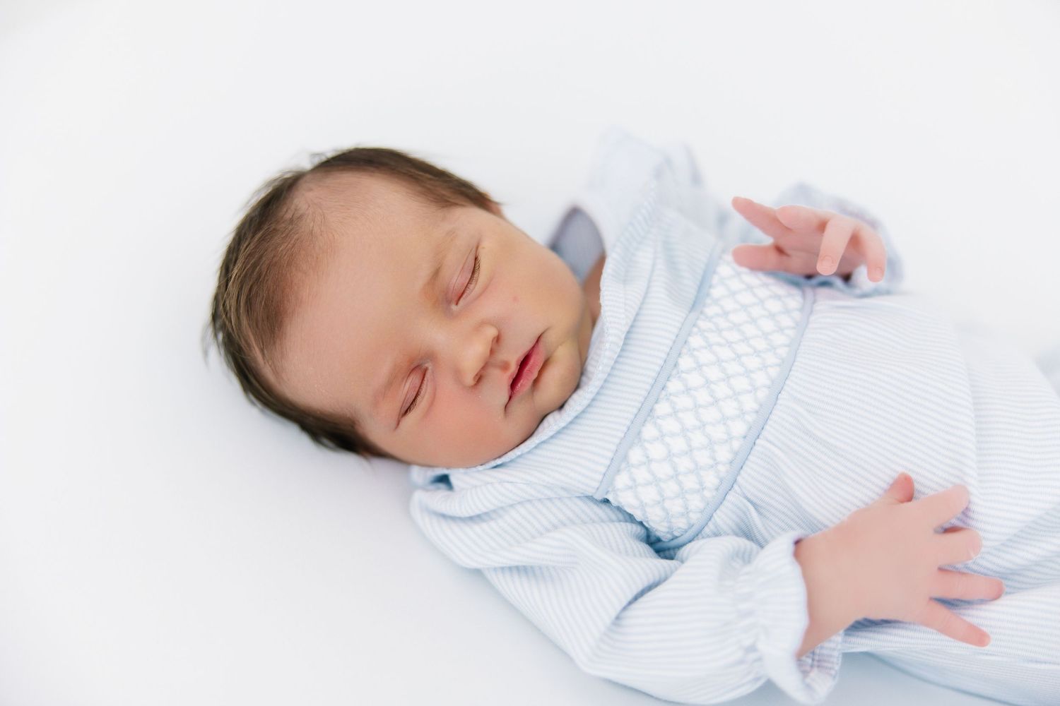 A peacefully sleeping newborn baby wearing light blue clothing rests on white bedding.