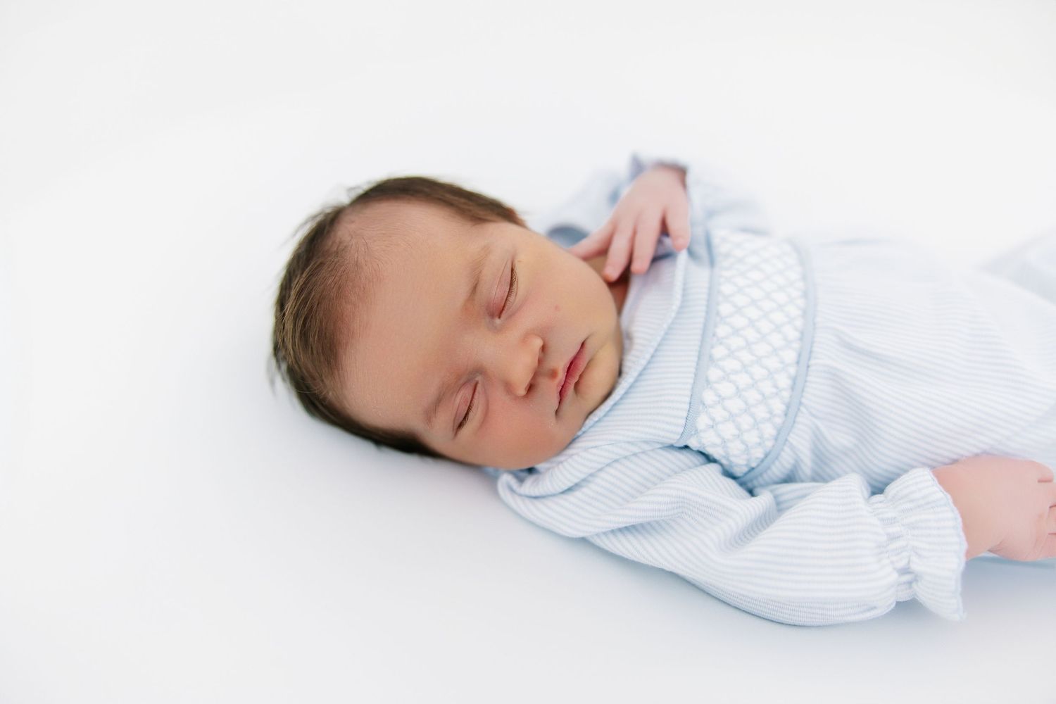 A peaceful sleeping infant wearing soft light blue clothing lies on a white background.