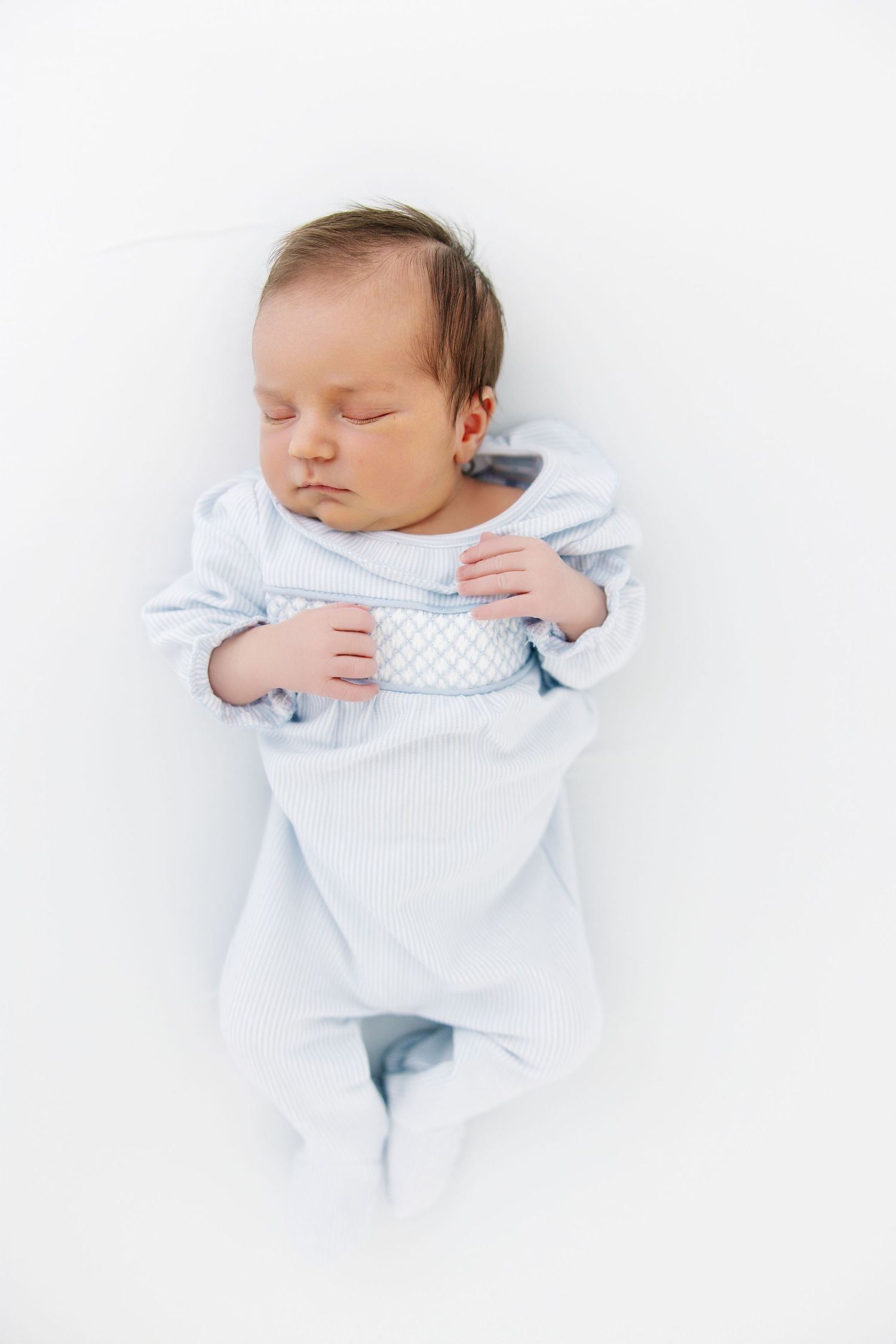 A sleeping newborn baby in light blue clothing lies peacefully against a white background.