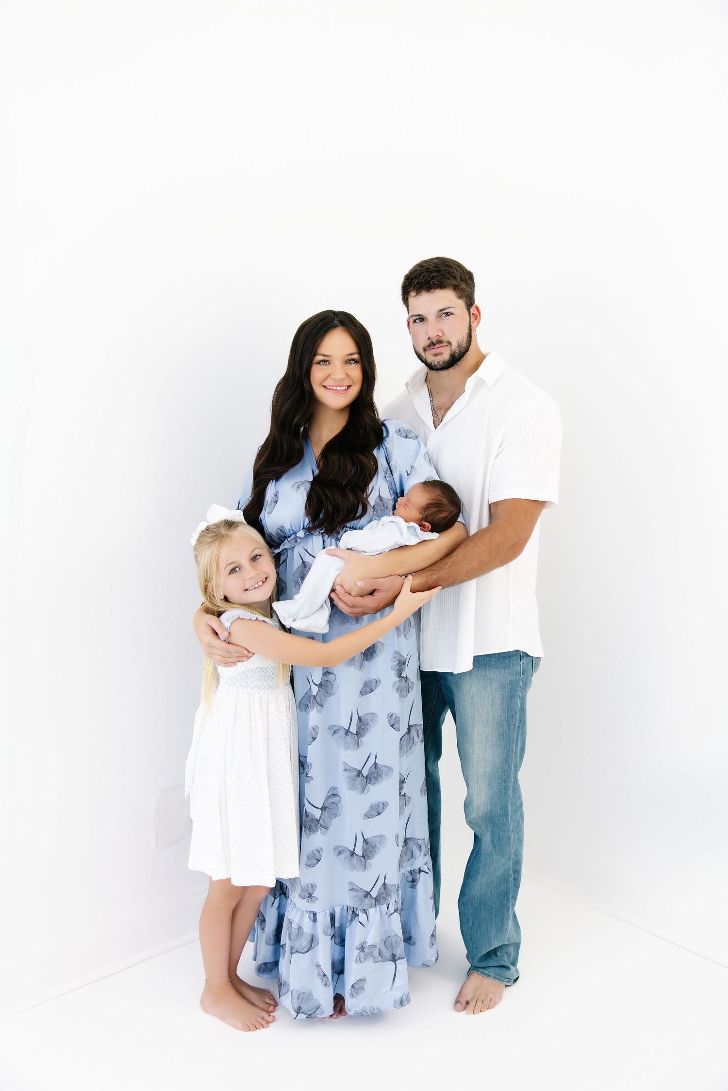 Family poses together in coordinating blue and white outfits against a white studio background.