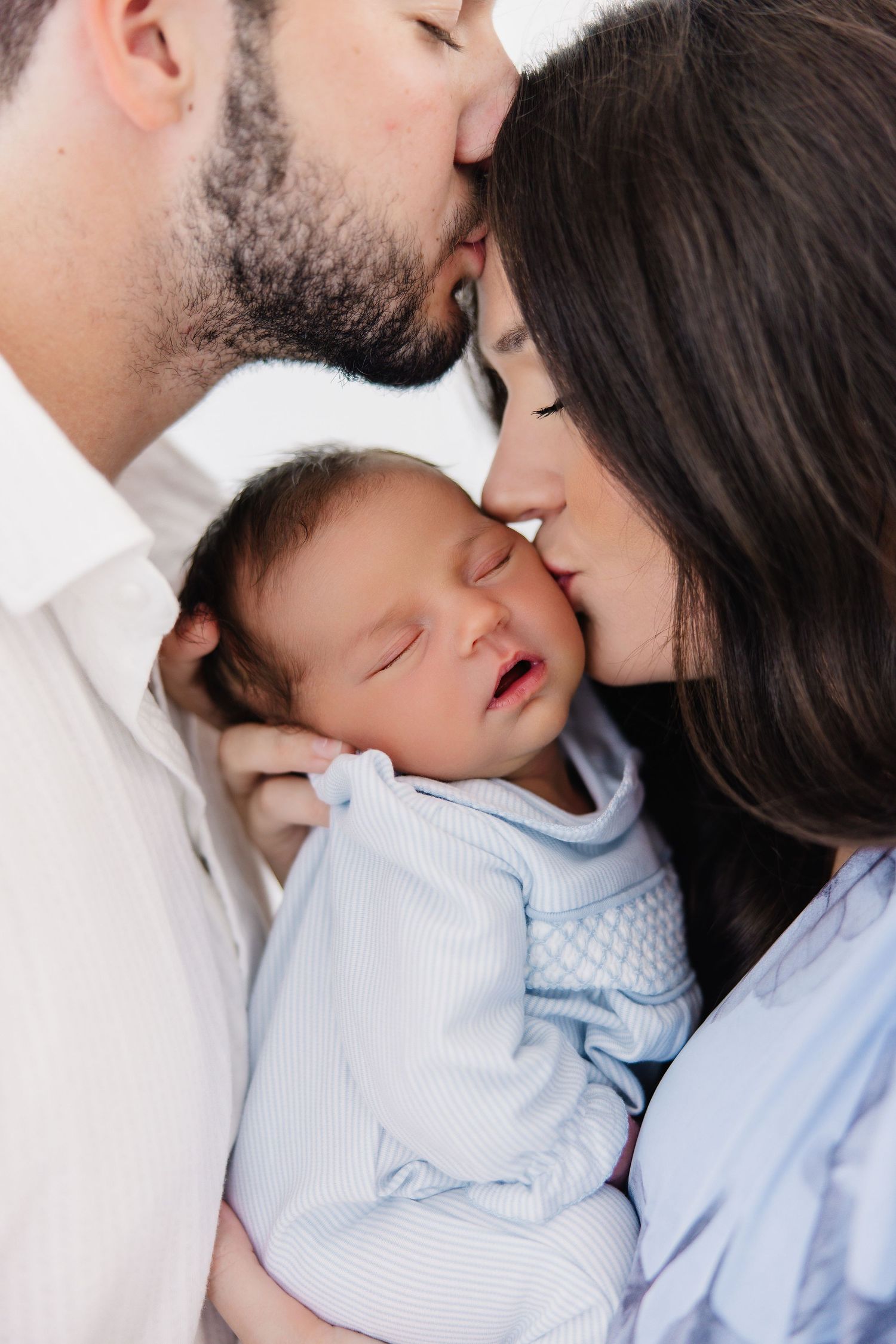 A tender family moment as parents kiss their sleeping newborn baby between them.