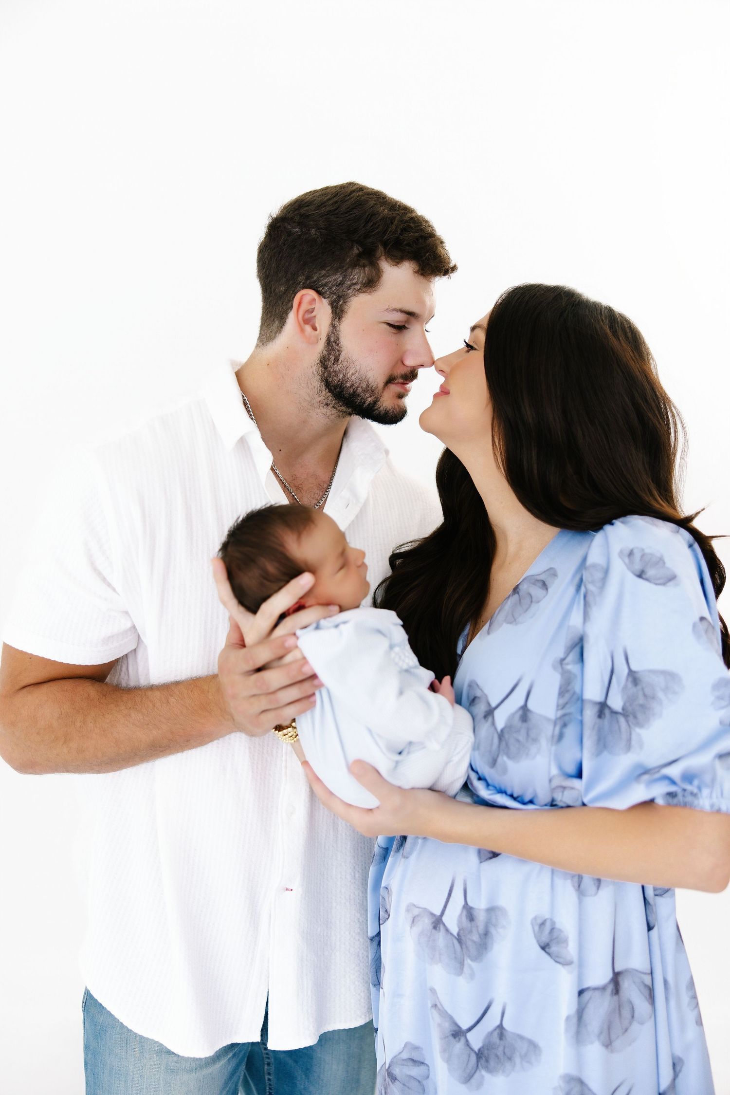 A series of intimate family photos showing parents cuddling with their newborn against a white backdrop.