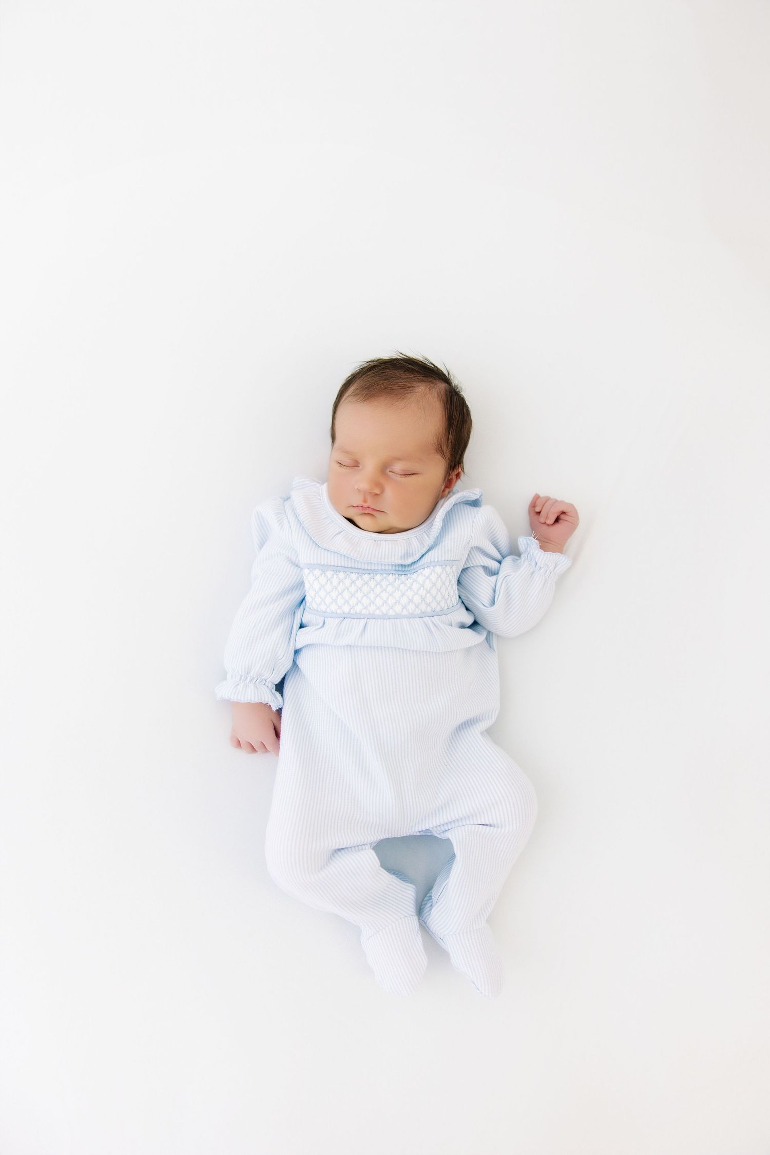 A sleeping newborn baby wearing light blue clothing photographed on a white background.