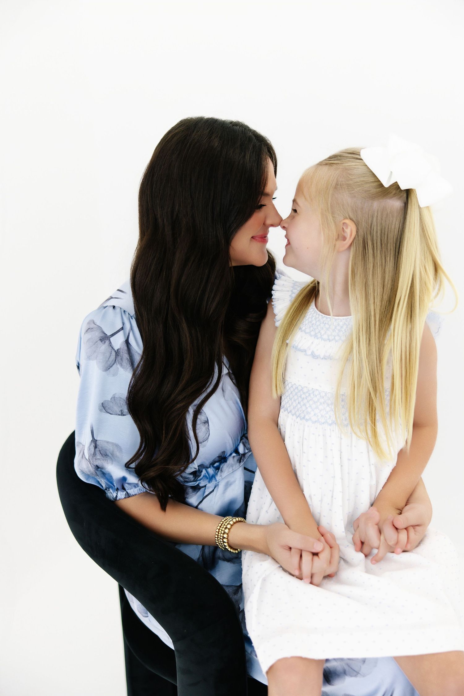 Playful interaction between mother and daughter in white clothing against white backdrop.
