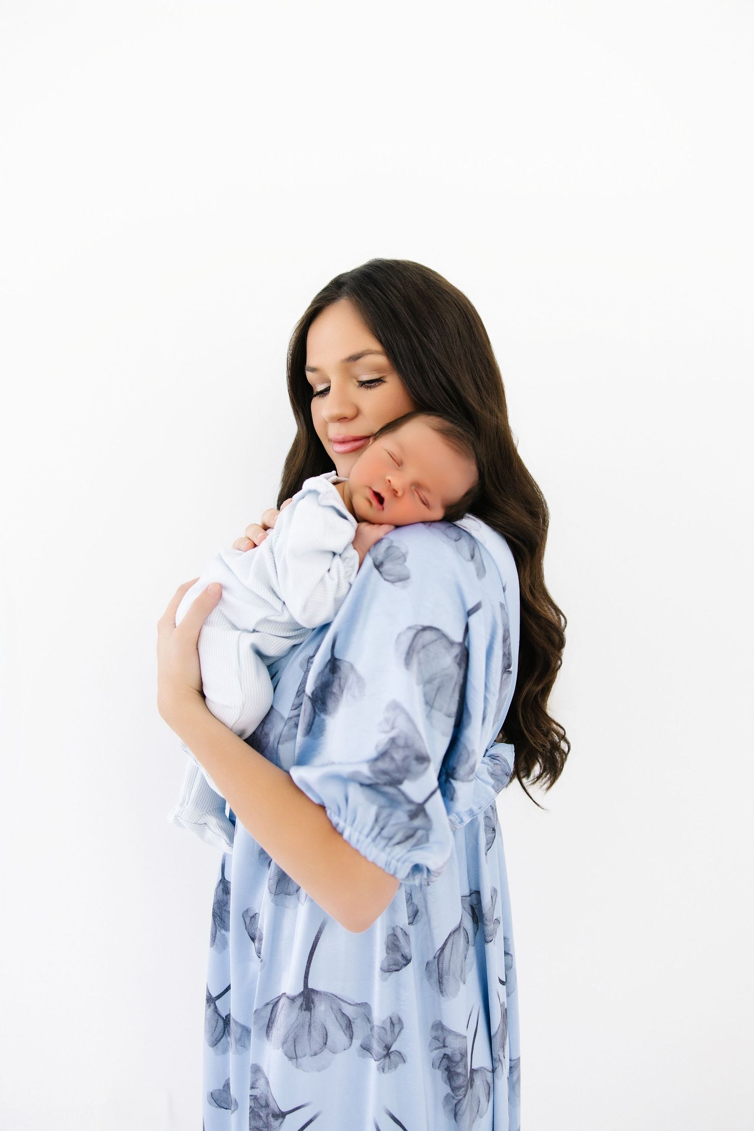A series of photos showing someone cradling a baby while wearing a light blue floral dress against a white background.