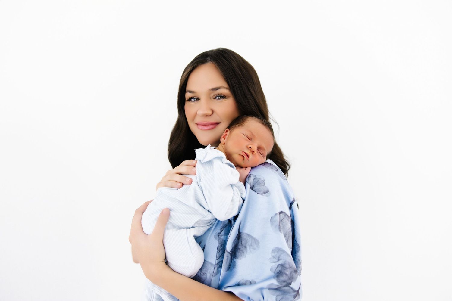 Peaceful mother and newborn baby together in soft white bedding resting after breastfeeding.