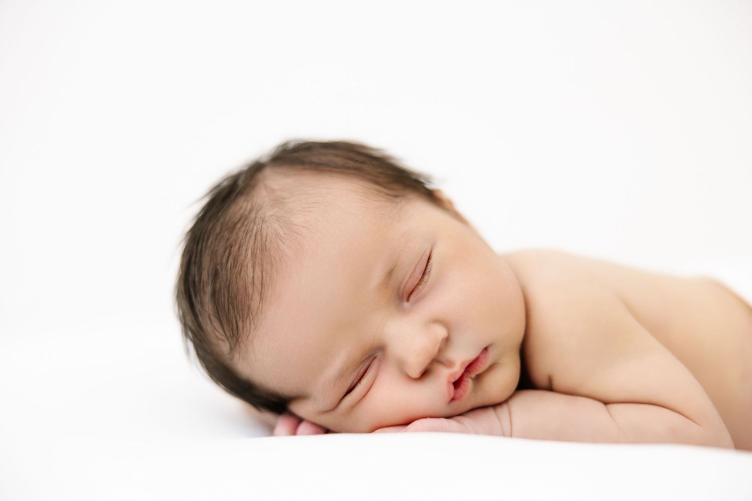 A peaceful sleeping newborn baby lies on a white surface in profile view.