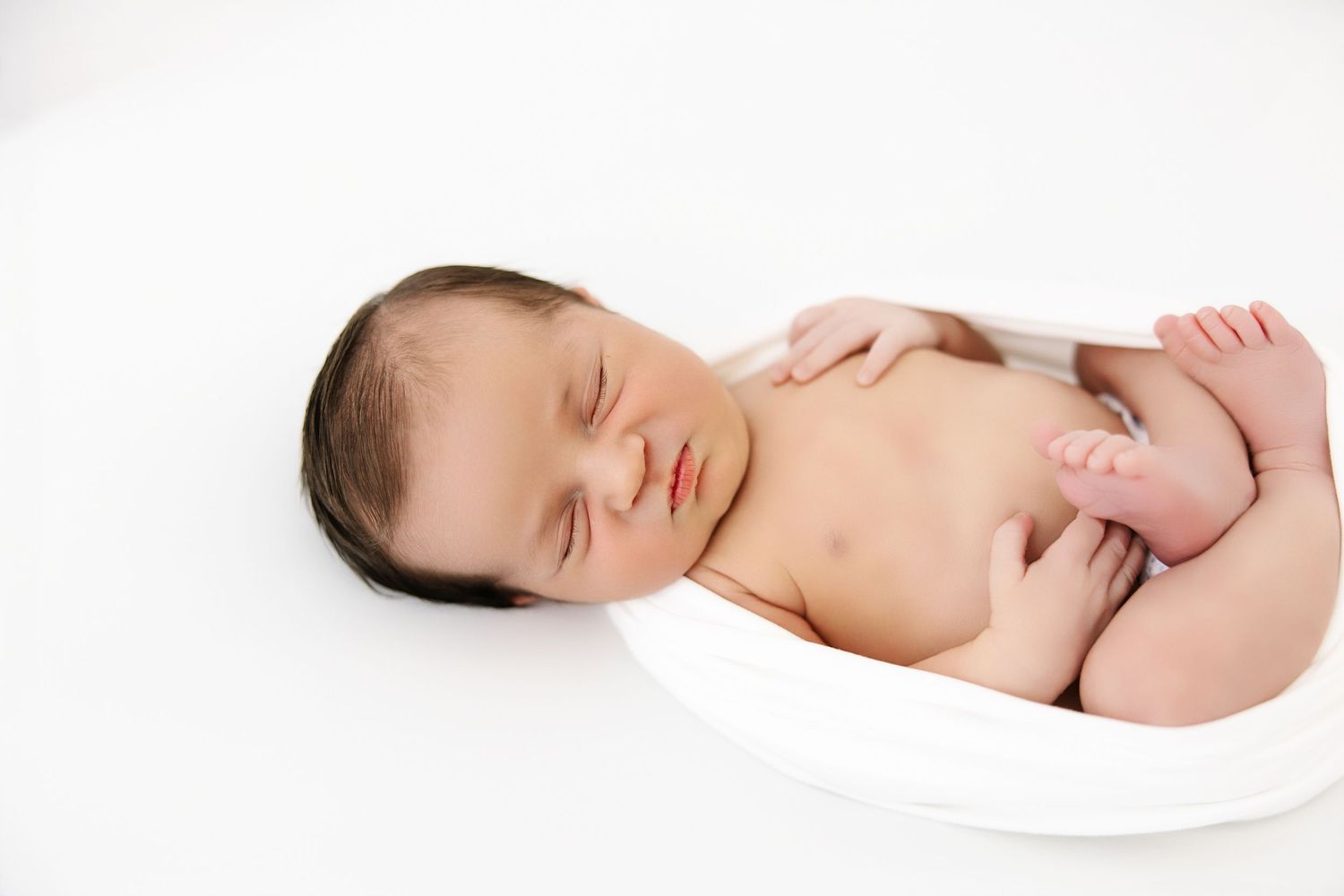 Three peaceful sleeping newborn babies in white wearing diapers are positioned in a horizontal line.