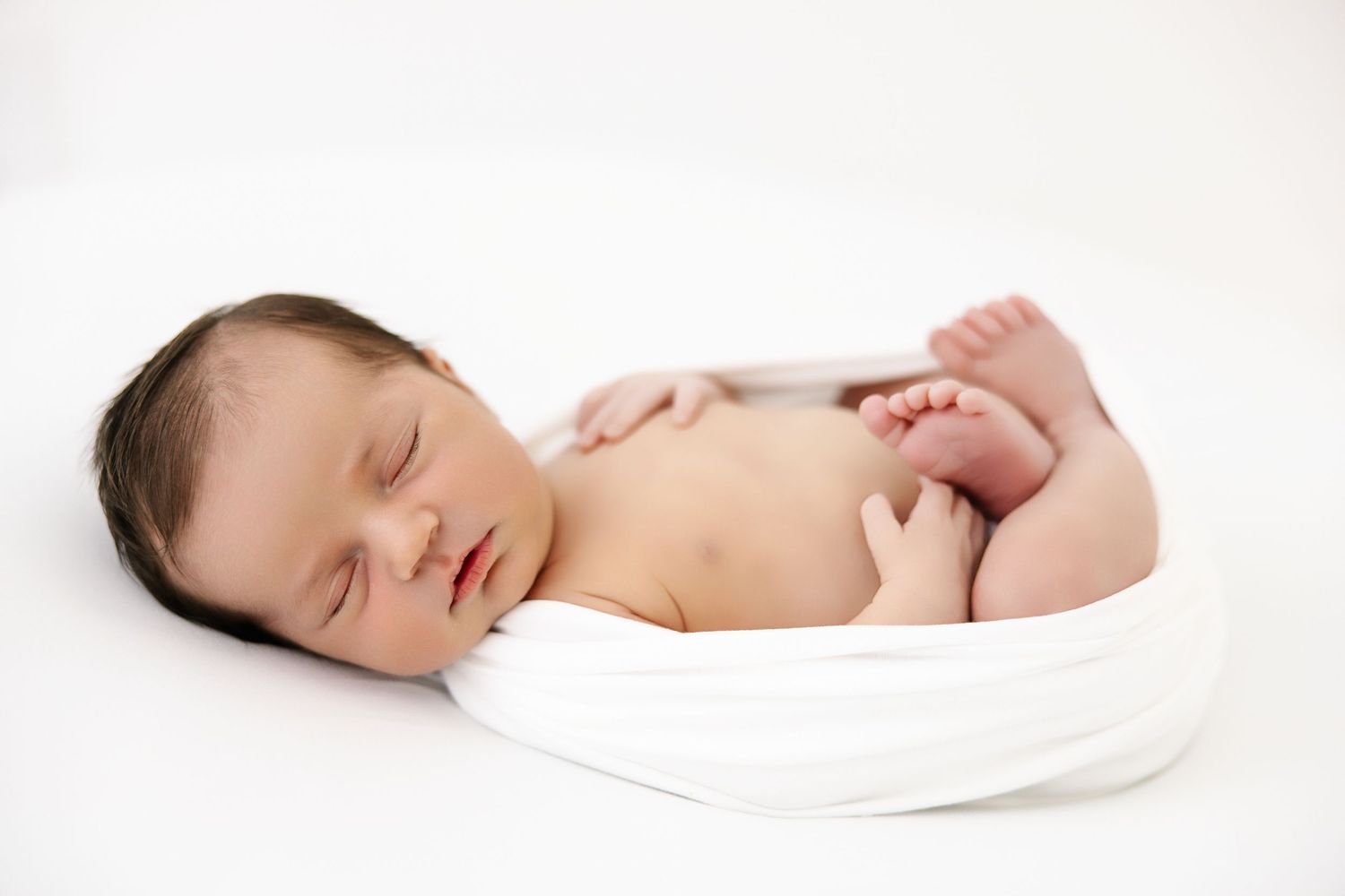 Peaceful sleeping newborn baby wrapped in white blanket against light background.