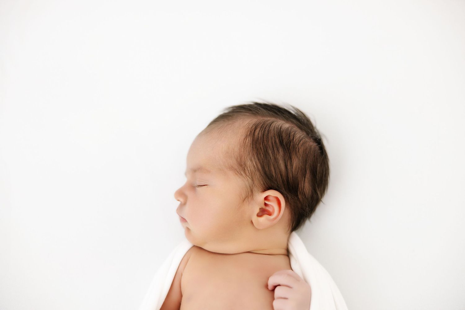 A peaceful sleeping newborn baby lies on a soft white background.