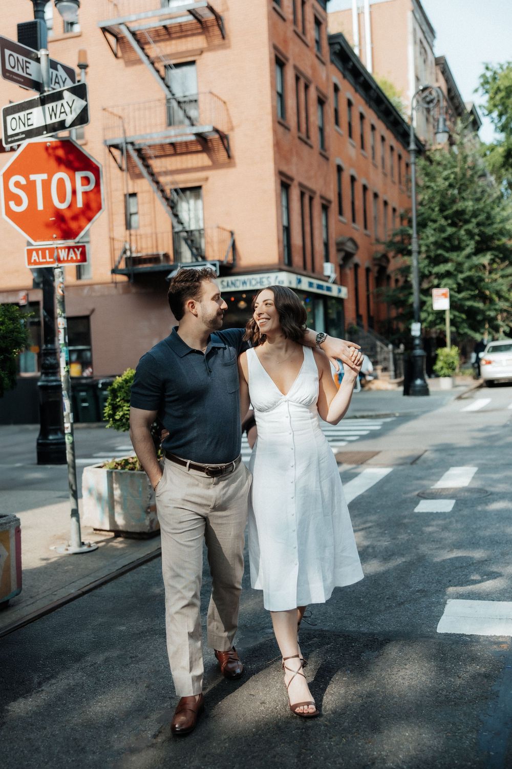 A couple strolls hand in hand down a brownstone-lined street in New York City.
