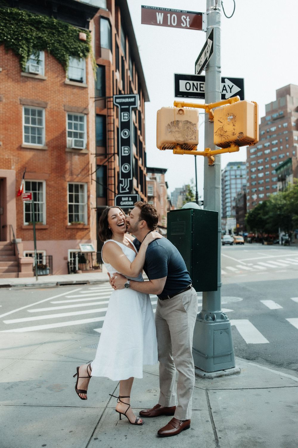 A couple shares a tender moment on a city corner with a street sign and traffic light in the background.