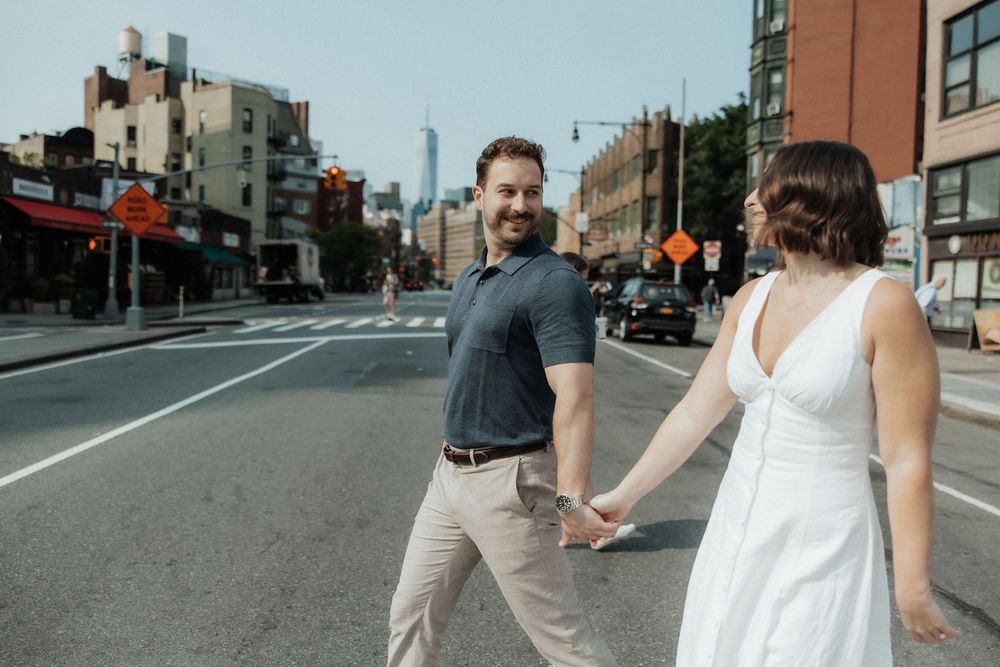 A couple holds hands while walking together on an urban street on a sunny day in casual attire.