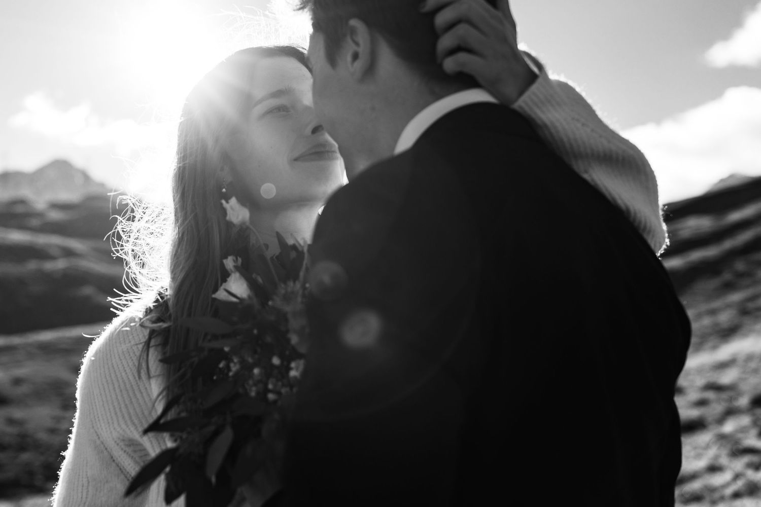 A romantic couple embraces in silhouette against a bright sky in this black and white wedding photograph.