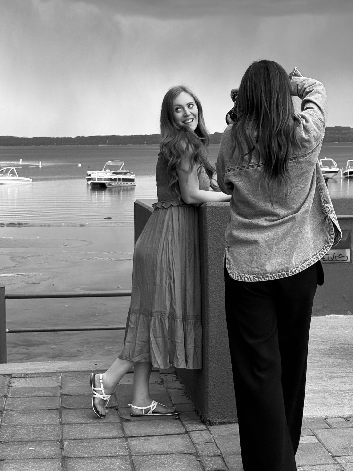 Photographer captures model in green dress posing by lake with boats during sunset photoshoot.