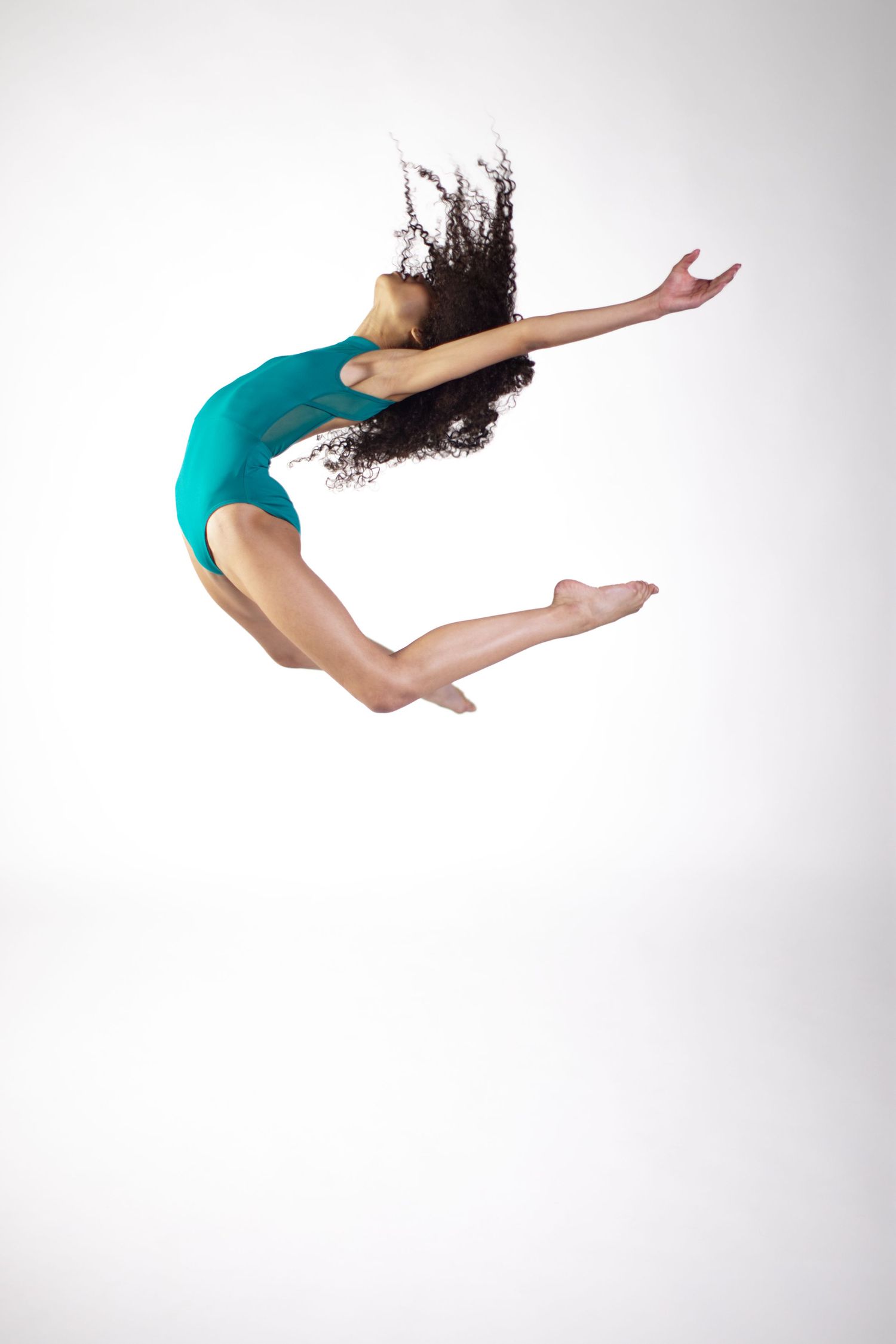 Dancer in black athletic wear performs graceful backbend movement against white background with curly hair flowing.