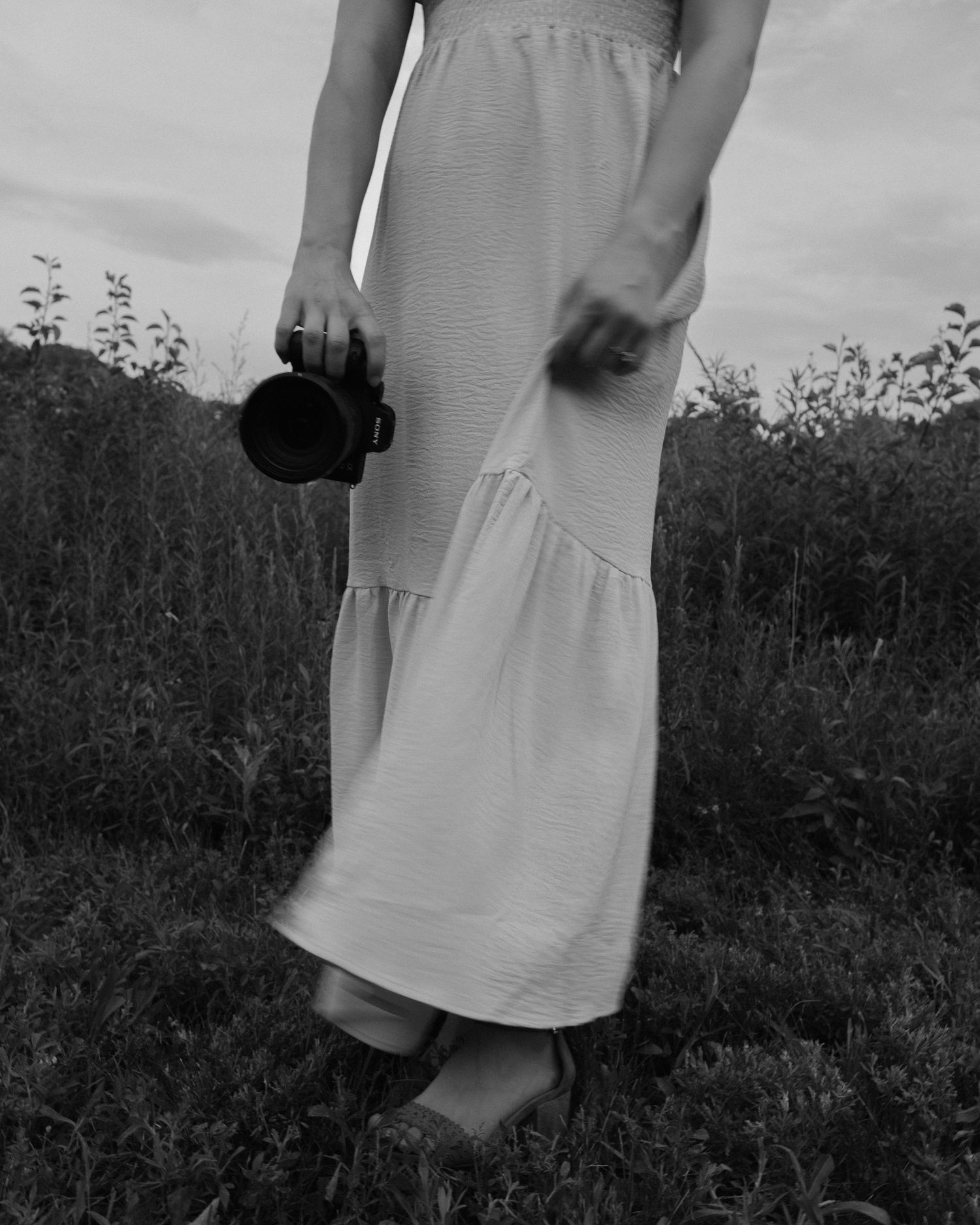 A person in a white summer dress stands in a meadow at multiple angles creating an artistic sequence in black and white.