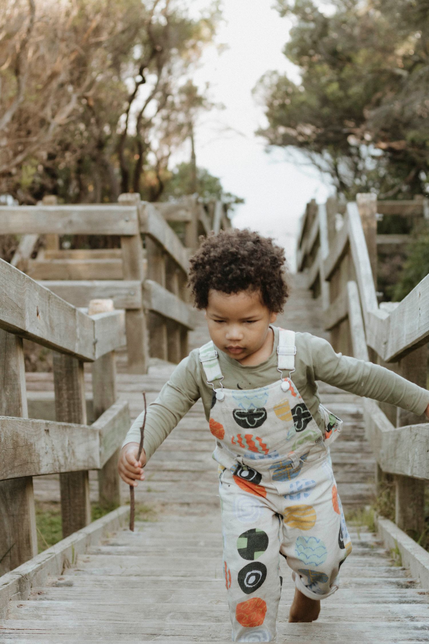 Child walking up wooden beach boardwalk stairs wearing patterned shirt.