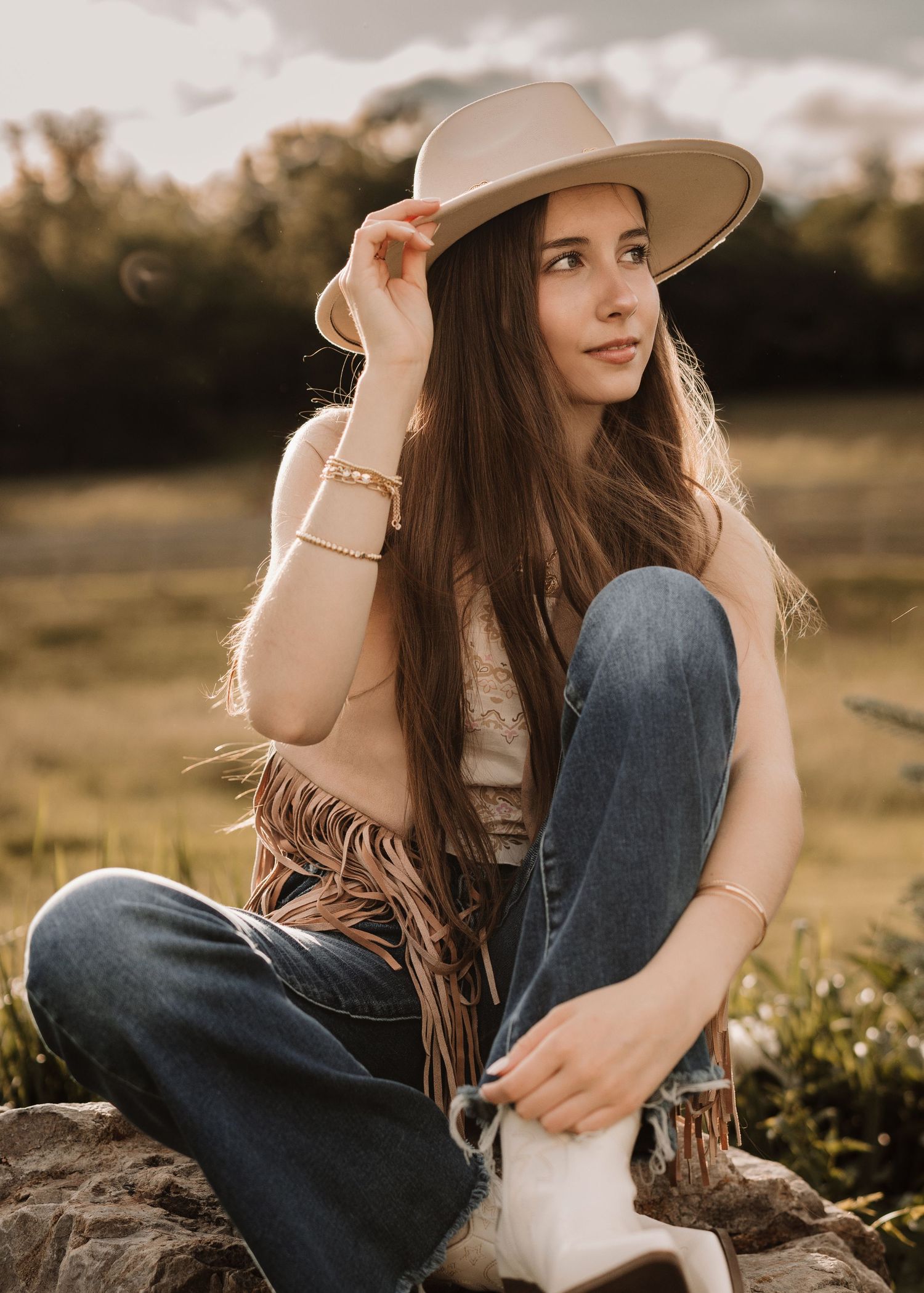 Western-inspired portrait with fringe jacket and hat in natural outdoor setting.