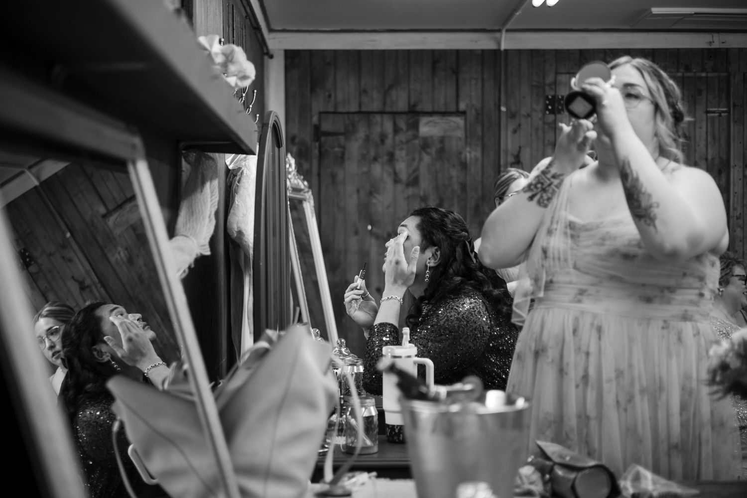 Black and white photograph of wedding party preparations showing people getting ready in a wooden room.