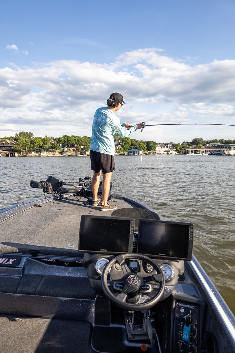 Bass boat dashboard and steering controls with lake view and cloudy sky in the background.