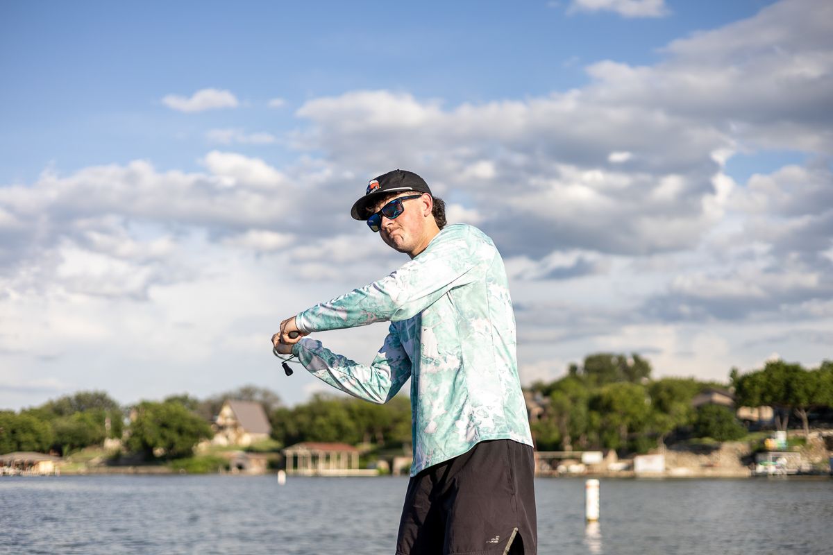 Angler in light colored shirt casting a fishing line on a lake with dramatic cloudy sky.