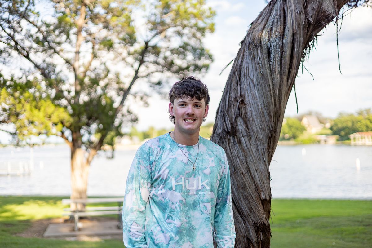 Youth sports team players in matching tie-dye blue shirts pose together on a sunny day in a park setting.