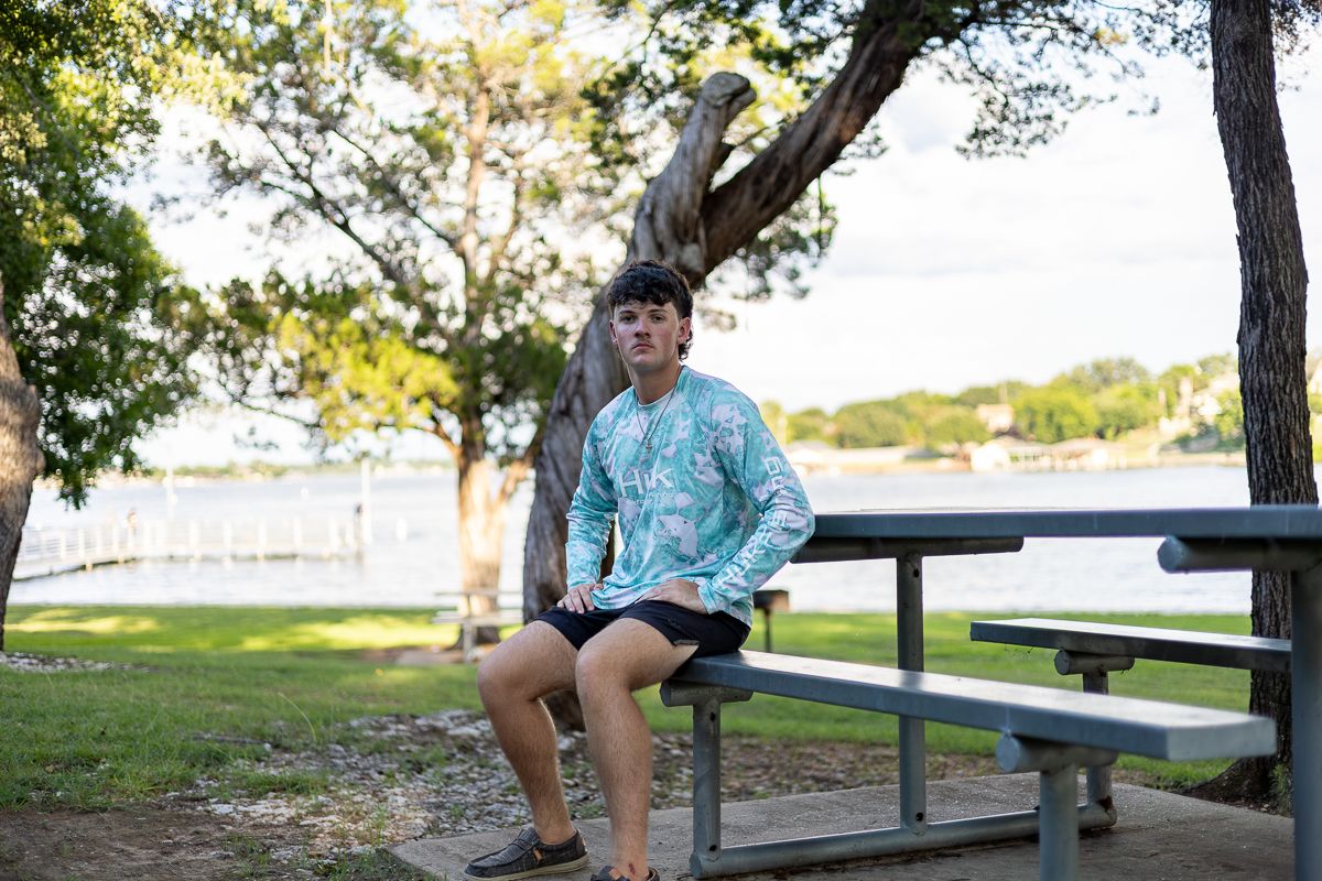 Someone sitting on a park bench near the water surrounded by trees on a sunny afternoon.