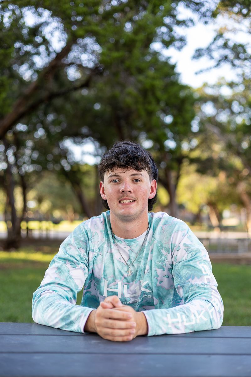 Student in a mint tie-dye sweatshirt sits at an outdoor picnic table with green trees in the background.