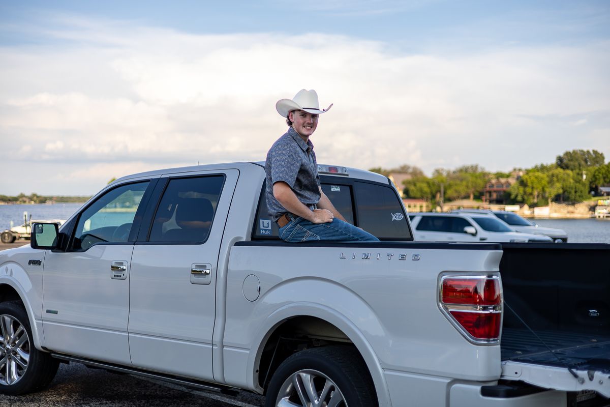 Person in cowboy hat sits in bed of white Ford F-150 pickup truck parked near waterfront at sunset.