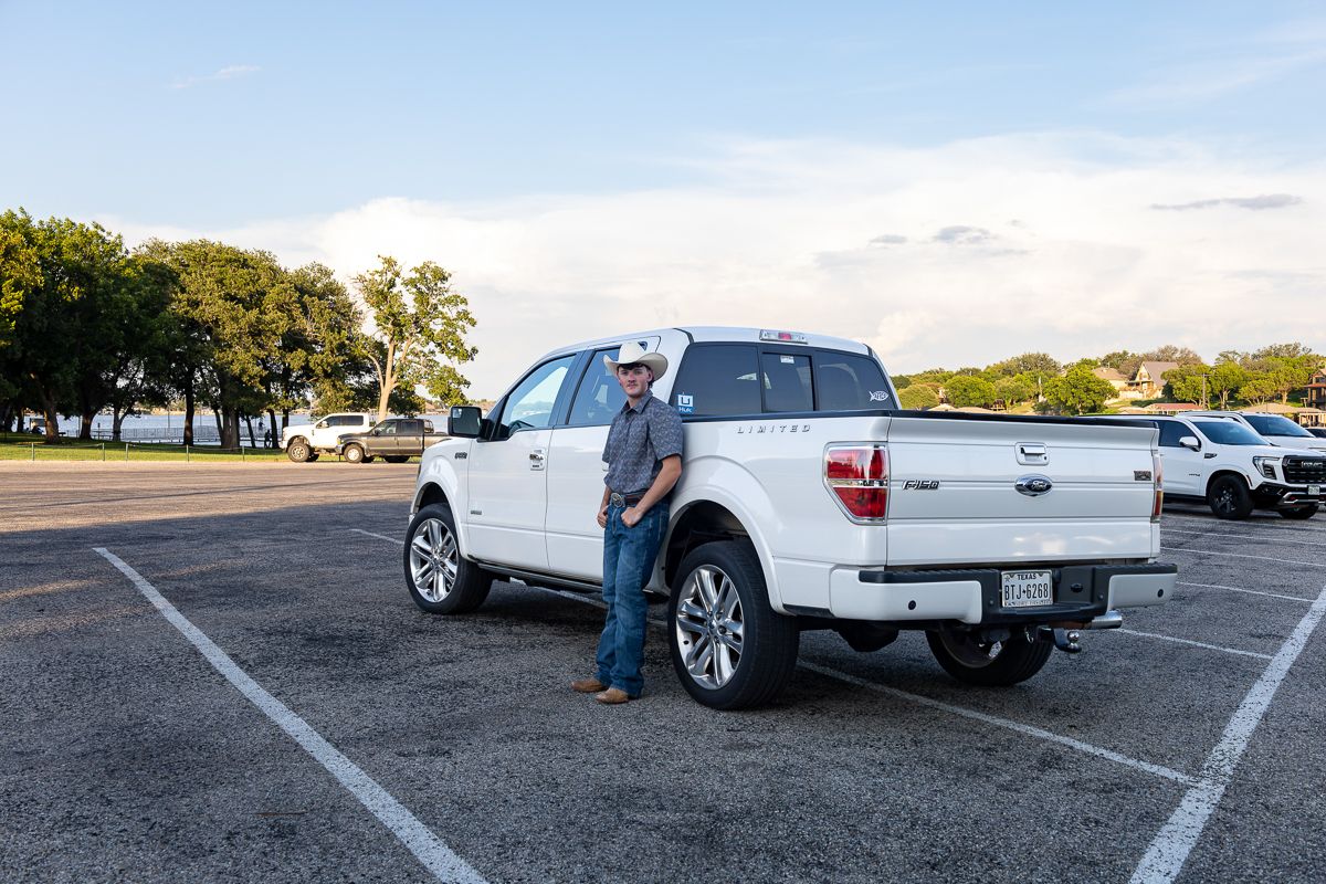Low angle view of white pickup trucks parked in a lot during sunset with trees in the background.