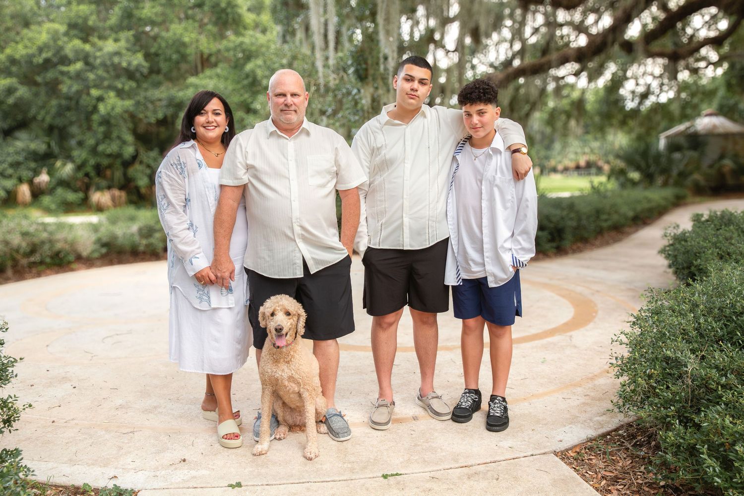 A family and their golden Labrador dog pose together on a winding garden path surrounded by lush greenery.