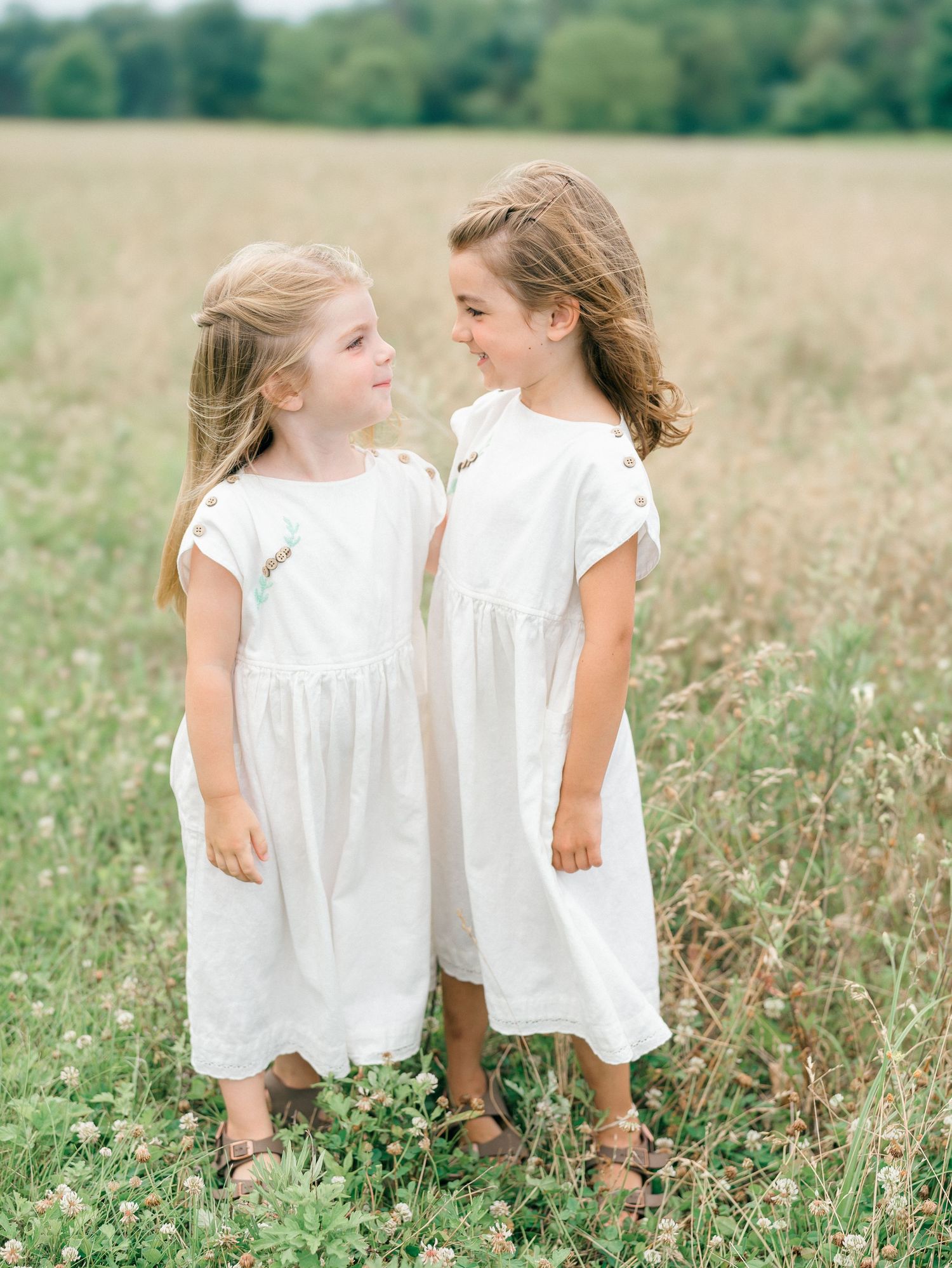 Two sisters embrace one other smiling.
