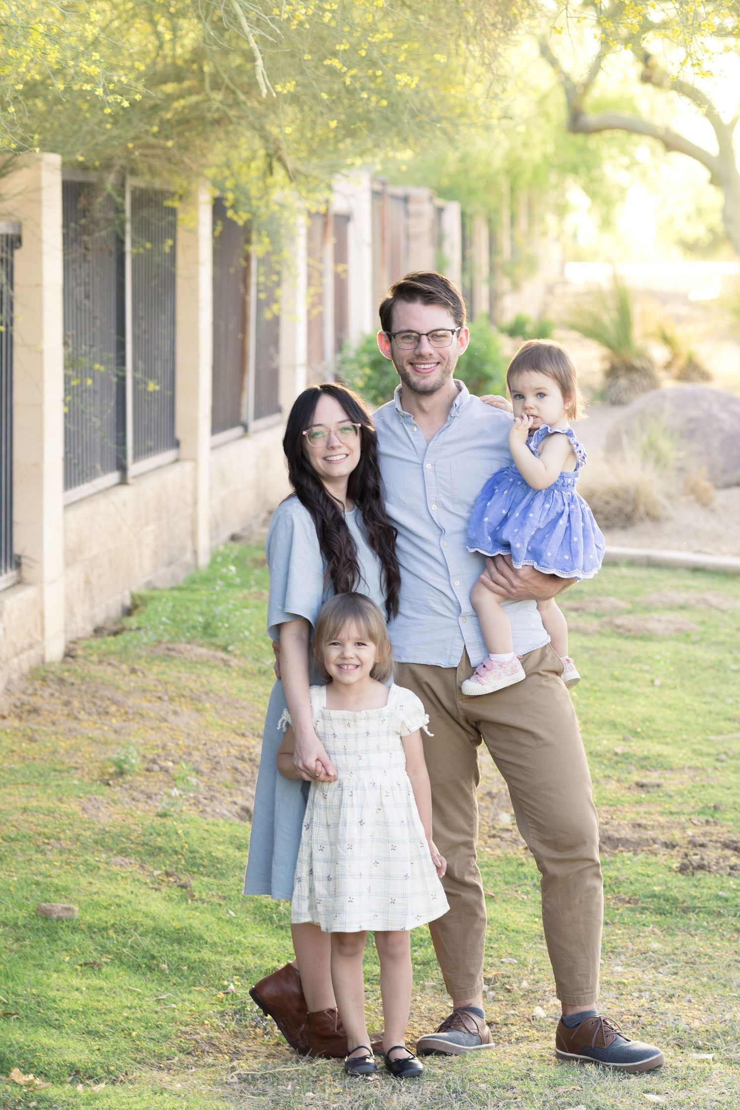 Family of four smiling with dad holding baby and mom holding toddler's hand in Queen Creek, AZ.