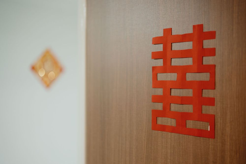 Red Chinese double happiness characters arranged in a row on a light wood paneled wall create a festive wedding decoration.