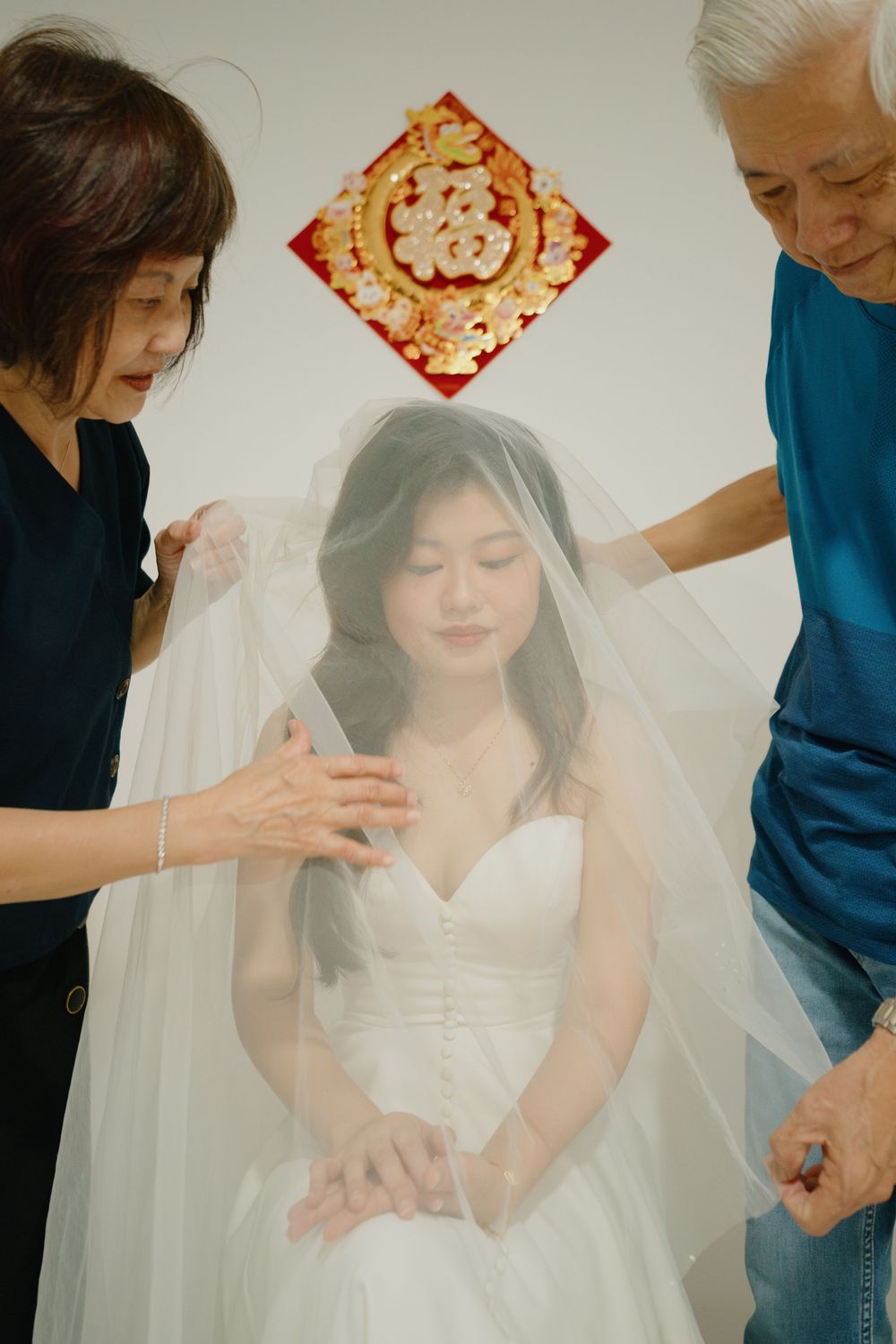 A wedding scene shows a bride in white dress getting ready with help adjusting her delicate veil in soft lighting.